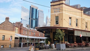 A hotel with a classic facade, a covered outdoor seating area, and a view of modern skyscrapers in the background. - Australian Heritage Hotel (The Rocks)