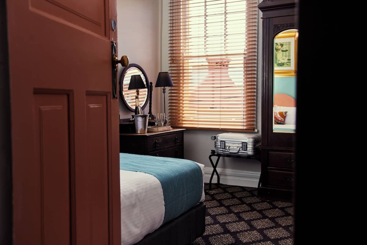 A bedroom with a bed, dresser, mirror, lamp, and a suitcase.