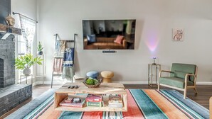 Een woonkamer met een open haard, een tv aan de muur, een groene fauteuil en een salontafel met gezelschapsspellen.