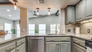 Een moderne keuken met granieten aanrechtbladen, roestvrijstalen apparatuur en lichtgrijze kastjes.