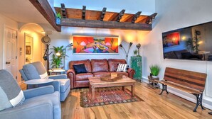 Un salon chaleureux avec un plafond en bois, un grand tableau, un canapé en cuir, une table basse et un banc.