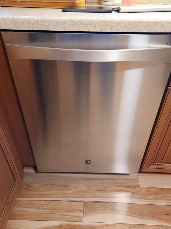 Un lavavajillas de acero inoxidable en una cocina con armarios de madera y una encimera con motas.