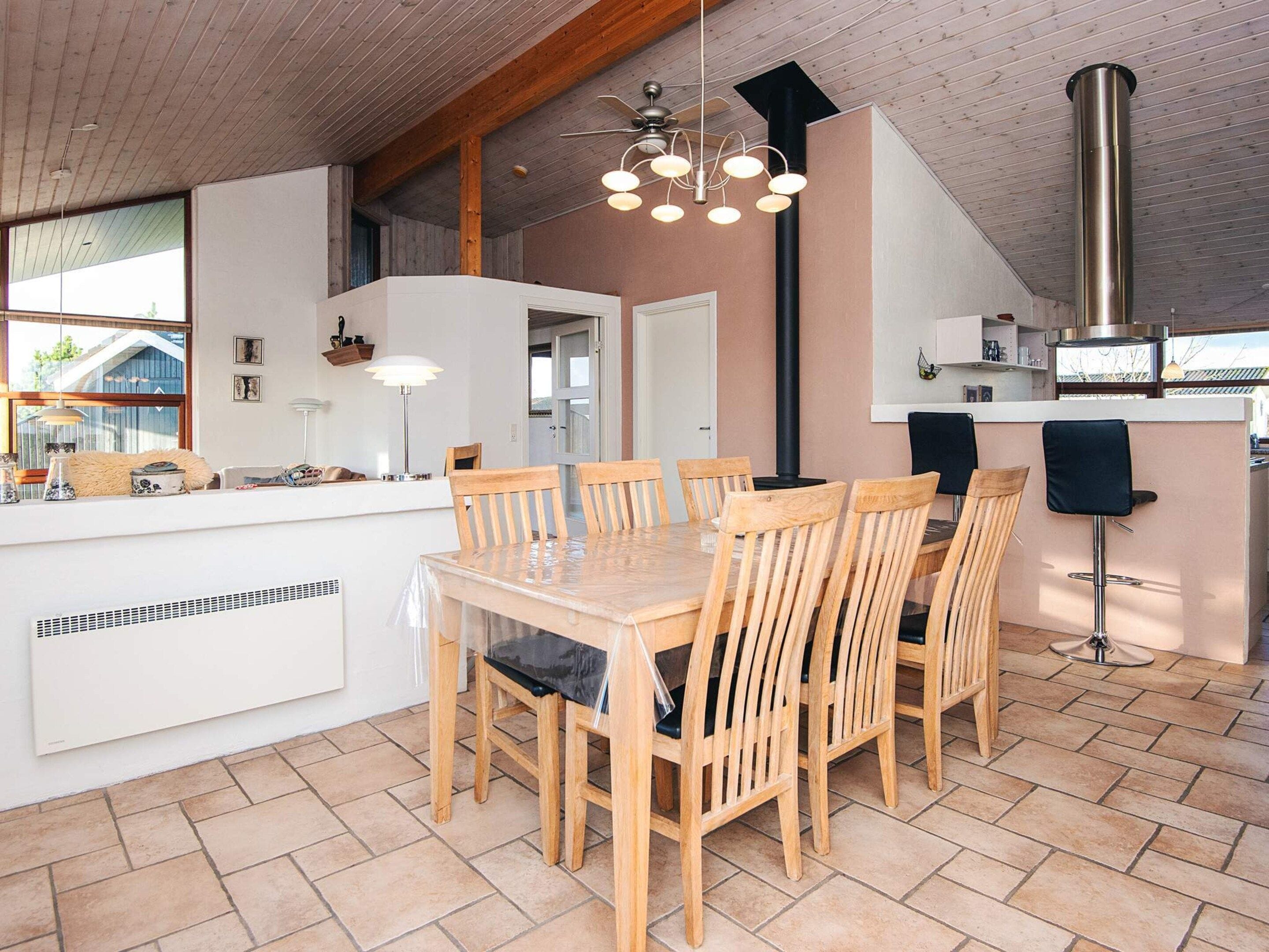Una cocina moderna con una isla central, sillas de madera, una estufa integrada y un ventanal grande.