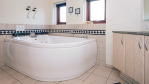 Un baño con una bañera grande, dos ventanas, salpicadero de azulejos y armarios de madera.