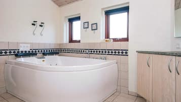 Casa de banho com uma banheira grande, duas janelas, painel de azulejos e armários de madeira.