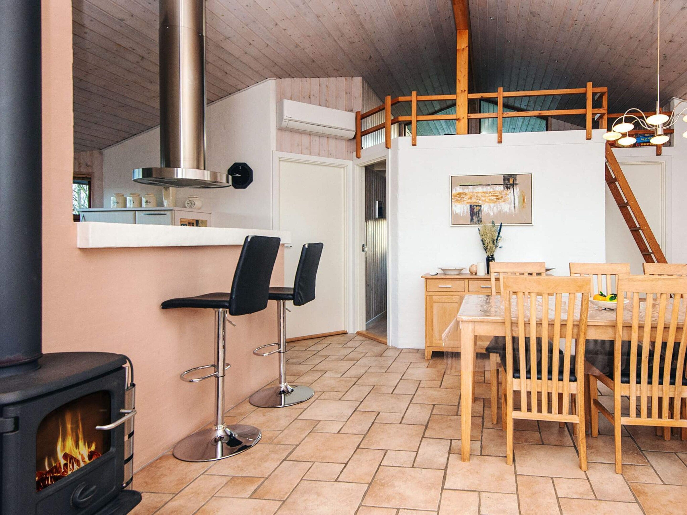 A cozy kitchen with a wood-burning stove, a dining area with wooden chairs and a table, and a loft bedroom with a wooden ladder.