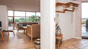 Amplia sala de estar con techo de madera, ventanas grandes, sofá, sillones, una mesita y televisor.