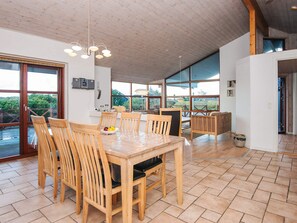 A spacious dining area with a wooden table and chairs, large windows offering a view of greenery, and a ceiling with exposed wooden beams. - 4 Star Holiday Home in Tarm (Tarm)