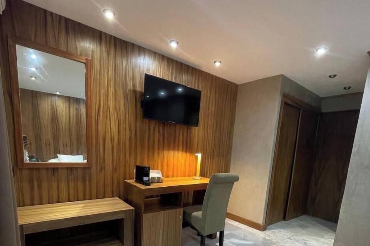 A modern room with a wooden wall panel, a flat-screen TV mounted above a desk, a chair, and a bench.
