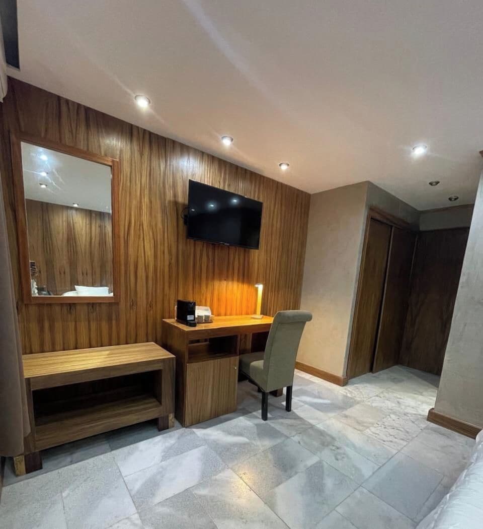 Una habitación moderna con un escritorio de madera, una silla, un televisor de pantalla plana montado en la pared y un espejo grande.