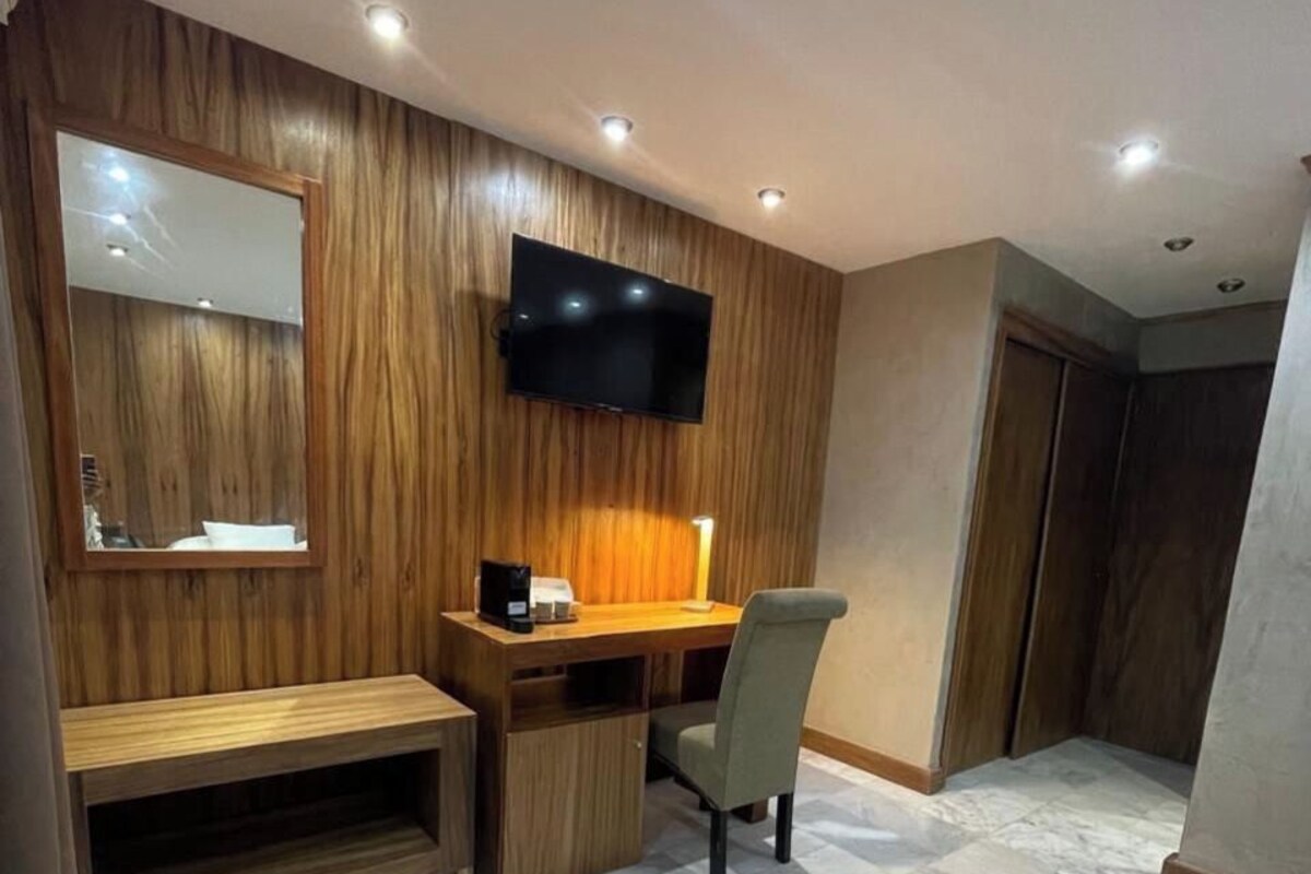 A modern room with a wooden wall panel, a flat-screen TV mounted above a desk, a chair, and a bench.