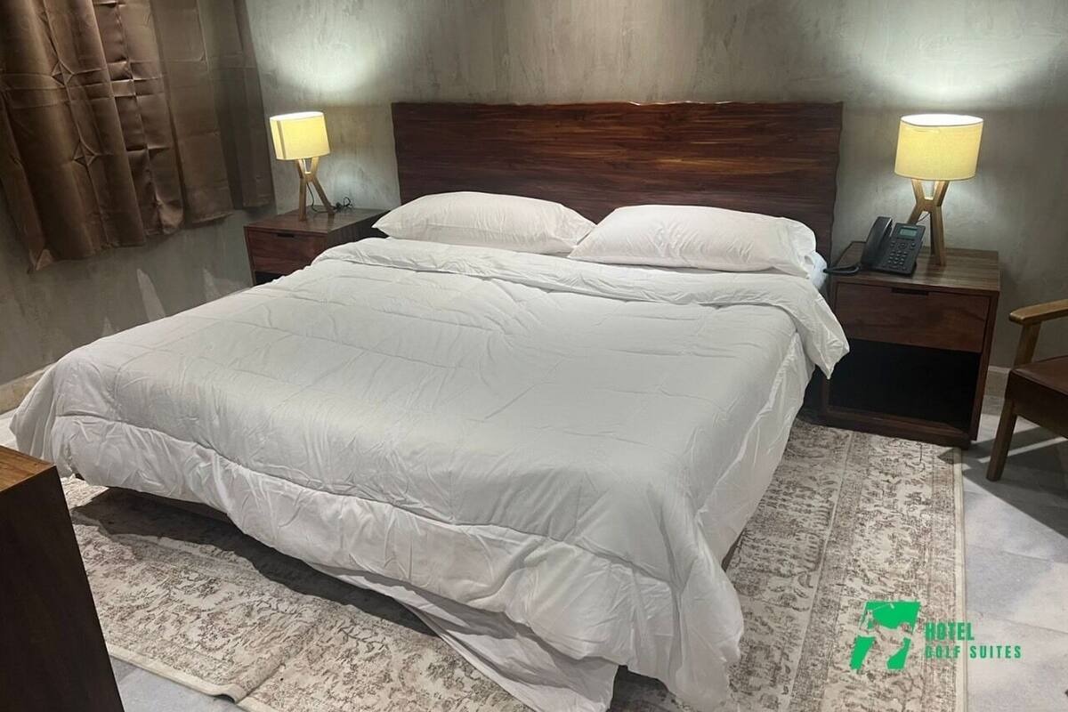 A hotel room with a large bed, two bedside tables with lamps, a telephone, and a rug.