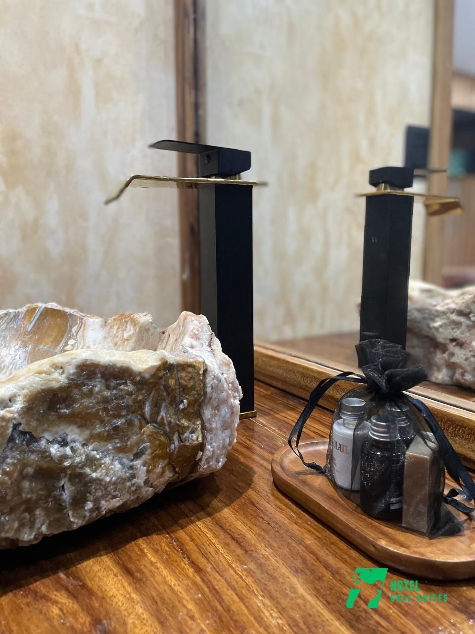 A rock centerpiece with a mirror reflecting a wooden table, a black candle holder, and a small gift bag with bottles.