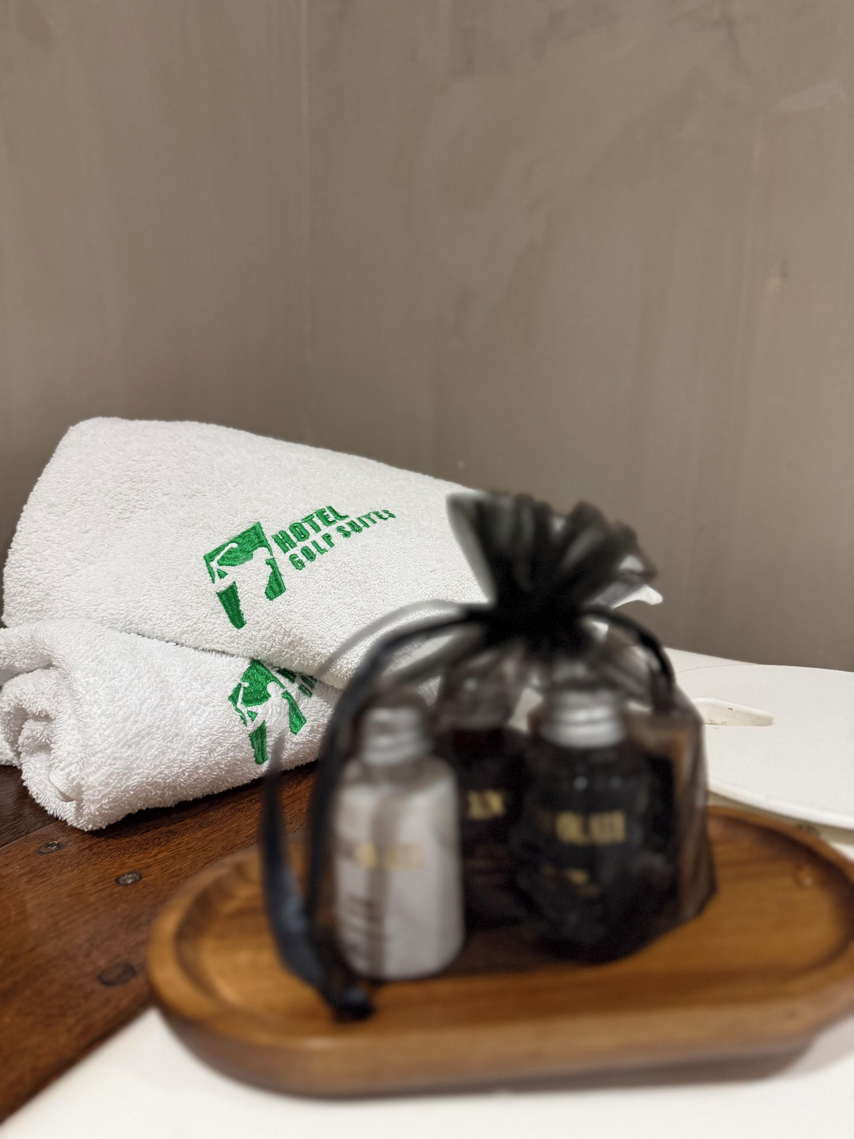 Une serviette blanche ornée d’un logo et d’un texte verts, un sac noir et un plateau en bois sur une table.