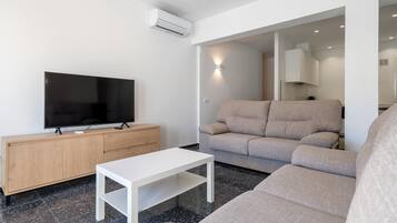 Una sala de estar moderna con un televisor de pantalla plana, un mueble de madera, una mesa de centro blanca y un sofá color beige.