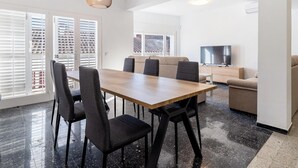 A modern living room with a dining area, featuring a wooden table, black chairs, a sofa, a TV, and a ceiling light. - Space with 5 bedrooms, 3 terraces and 150m beach (Platja d'Aro)