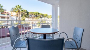A balcony with a round table and four chairs, overlooking a coastal town with buildings and palm trees. - Space with 5 bedrooms, 3 terraces and 150m beach (Platja d'Aro)