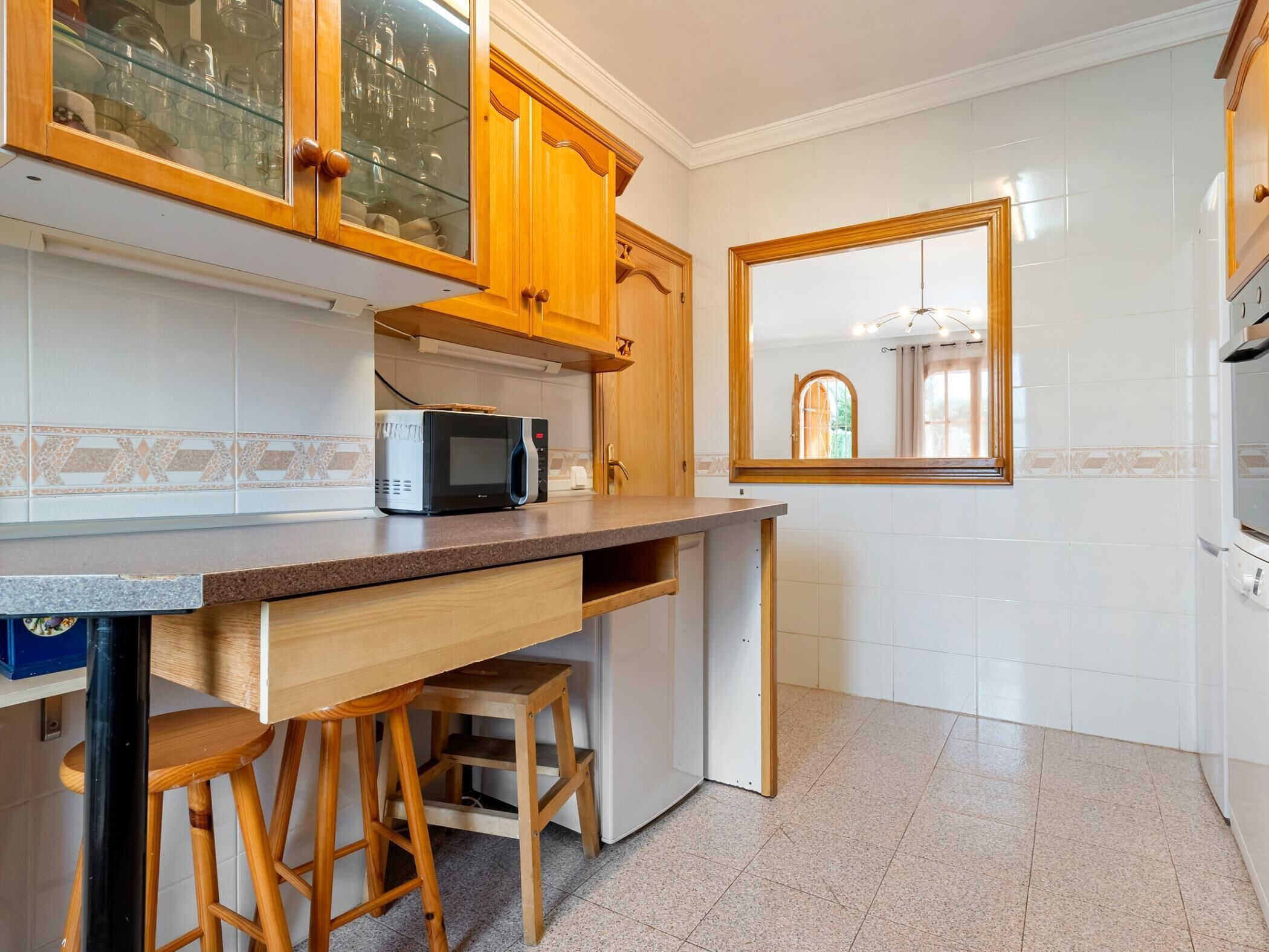 A kitchen with wooden cabinets, a microwave, a small refrigerator, and a bar stool.