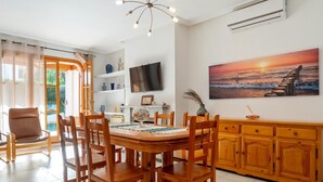 Una zona de menjador amb una taula i caires de fusta, un televisor fixat a la paret, i un quadre d'un tramuntana.