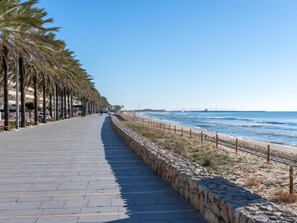 A paved walkway lined with palm trees, leading to a beach with a stone wall and wooden fence. - House 100m beach with 2 pools and barbecue (Calafell)
