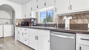 A modern kitchen with white cabinets, a stainless steel dishwasher, and a granite countertop. - Sparn Mountain Hideaway 3 Bedroom Home (Grand Junction)