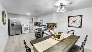 A modern kitchen with white cabinets, a stainless steel refrigerator, and a dining area with a wooden table and chairs. - Sparn Mountain Hideaway 3 Bedroom Home (Grand Junction)