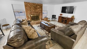 A living room with a brick fireplace, leather sofas, a coffee table, and a TV mounted on the wall. - Sparn Mountain Hideaway 3 Bedroom Home (Grand Junction)