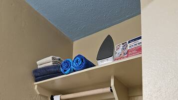 A corner of a room with a beige wall, a blue ceiling, and a shelf with folded towels and a first aid kit.