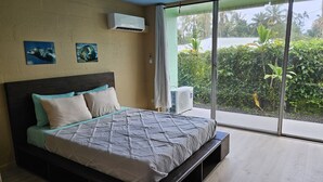 A bedroom with a large bed, a ceiling fan, and a view of greenery through the window.