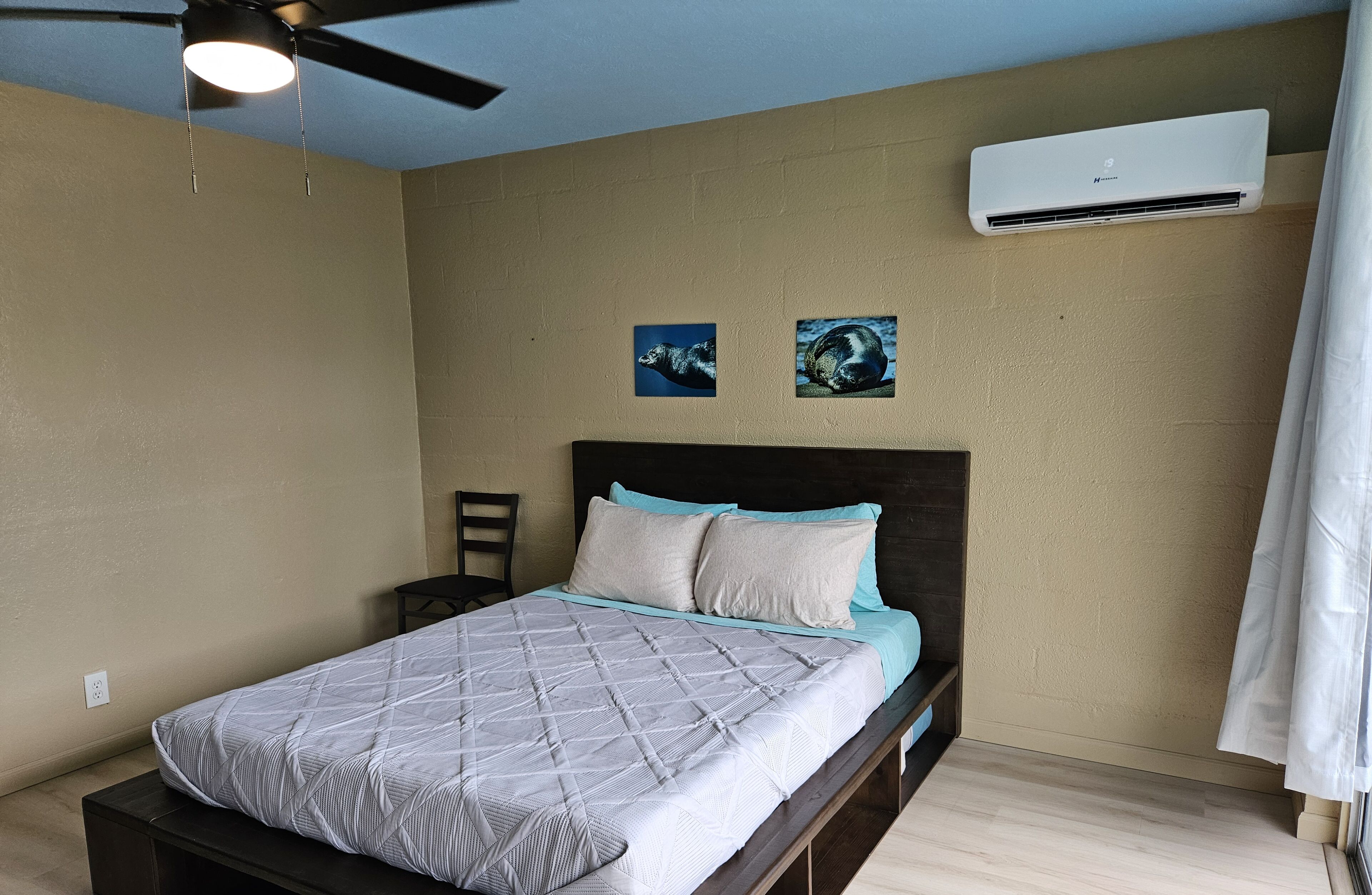 A bedroom with a bed, a ceiling fan, an air conditioning unit, and two wall-mounted pictures.
