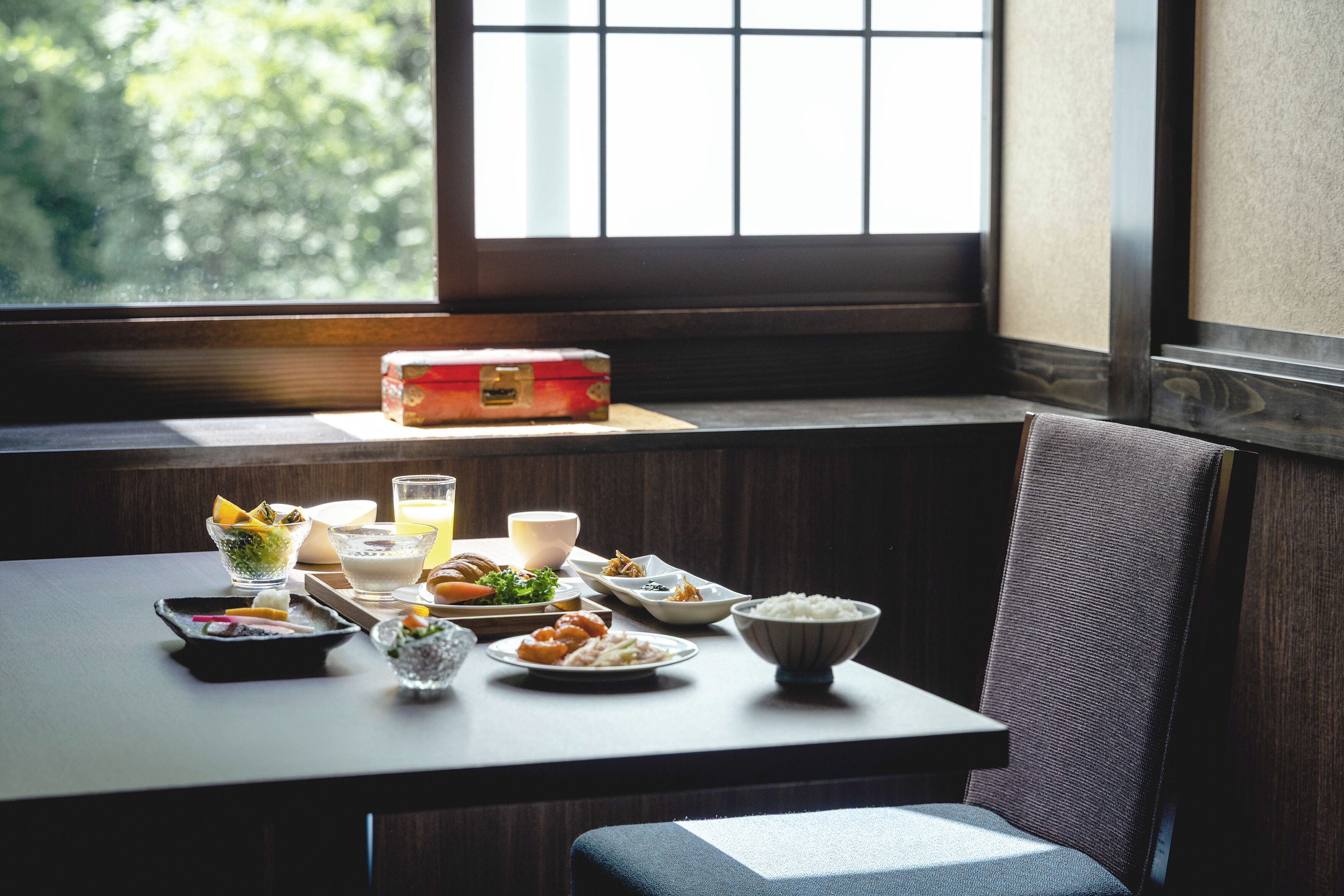 A dining table with various dishes and a glass of juice, set in a room with a window and a wooden bench.