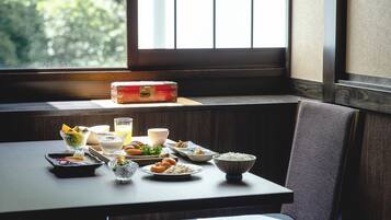 A dining table with various dishes and a glass of juice, set in a room with a window and a wooden bench.