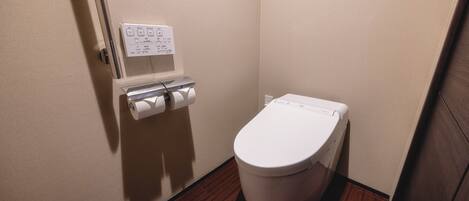 A small, clean bathroom with a toilet, a paper towel dispenser, and a hand dryer.