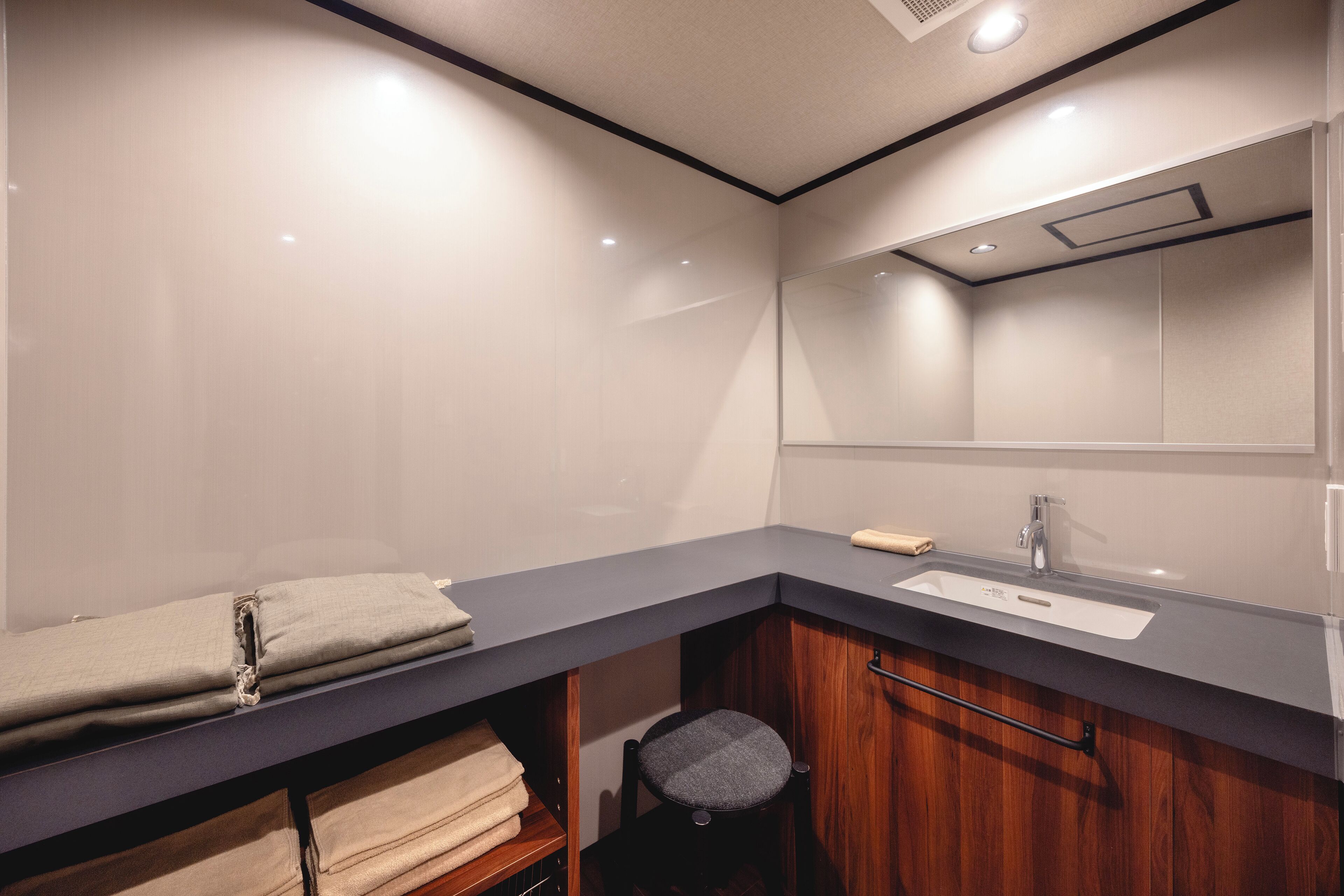 Un baño moderno con encimera oscura, un lavabo y un espejo. Hay un perchero y una estantería con toallas dobladas.