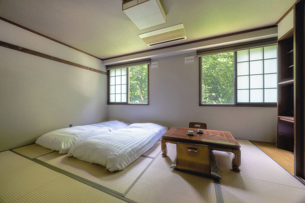 Une pièce de style japonais traditionnel, avec un sol recouvert de tatamis, un futon servant de lit, une table en bois et des portes coulissantes.