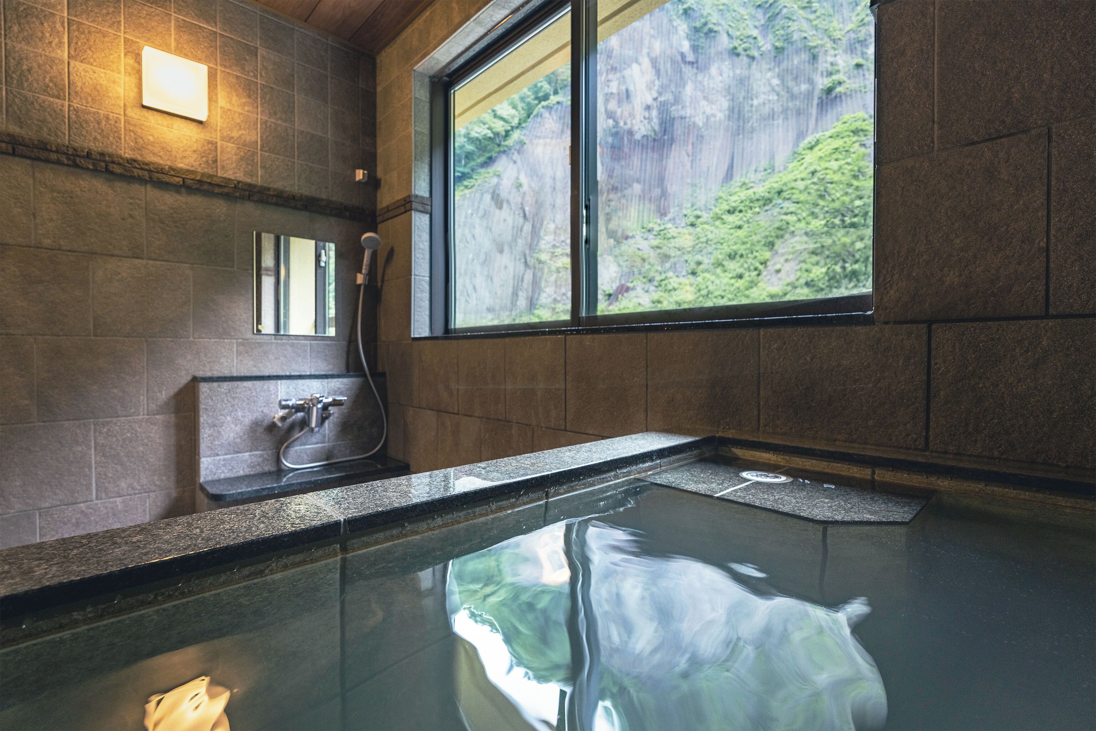 A hot spring bath with a view of a rocky cliff and greenery.