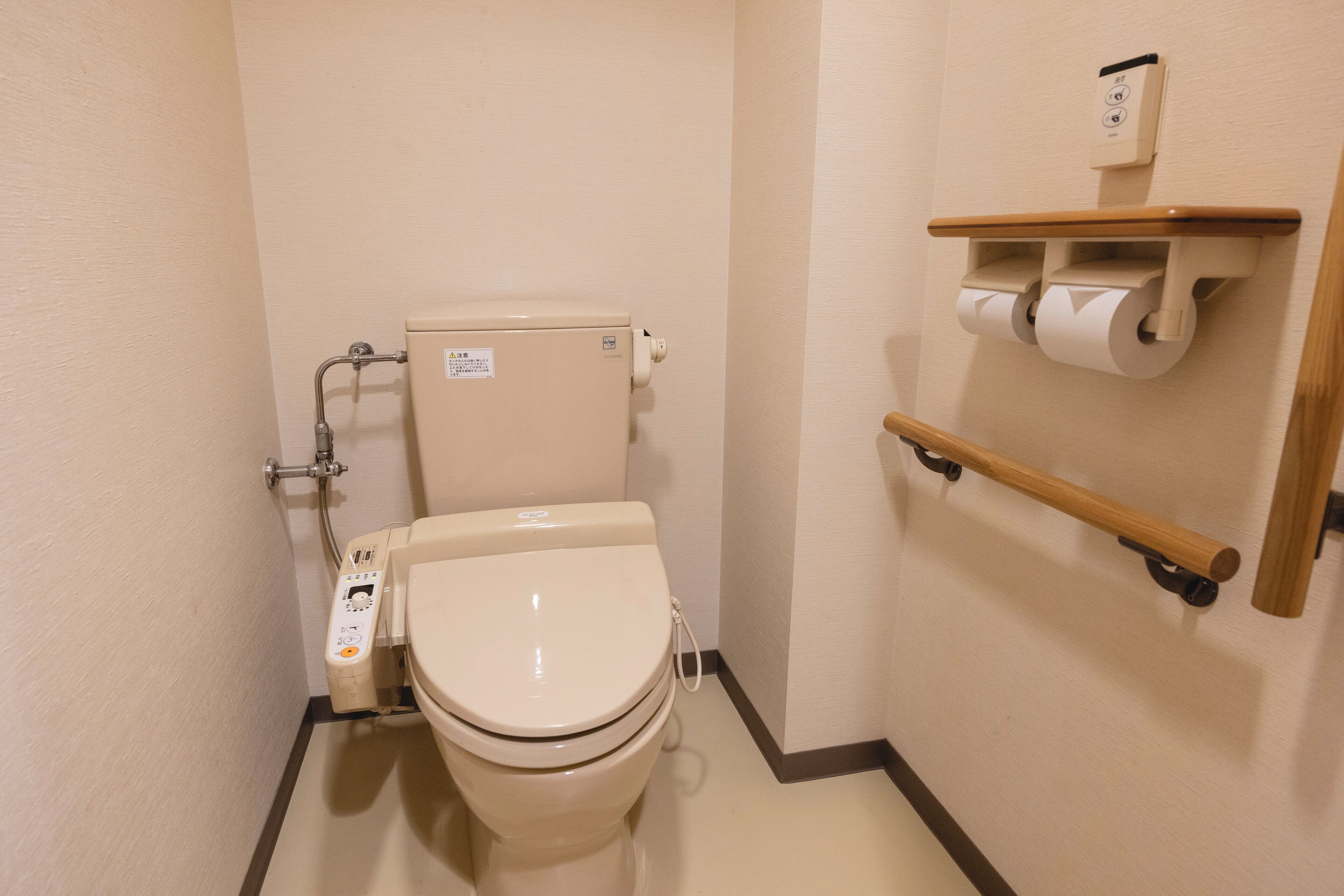 A small, modern bathroom with a toilet, a hand sanitizer dispenser, and a toilet paper holder on a wall-mounted shelf.