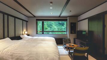 Ein Hotelzimmer mit einem großen Bett, einem Fernseher, einem kleinen Tisch und Blick auf Grün hinter einem Fenster.