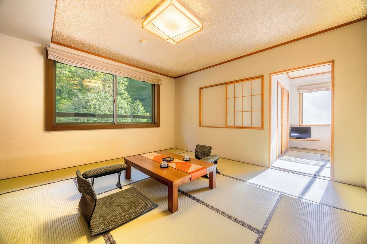 Une pièce traditionnelle japonaise avec un sol recouvert de tatamis, une table basse, une chaise et une porte coulissante donnant sur une autre pièce.