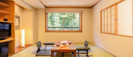 A tatami room with a low table, two cushions, a television, and a sliding door.