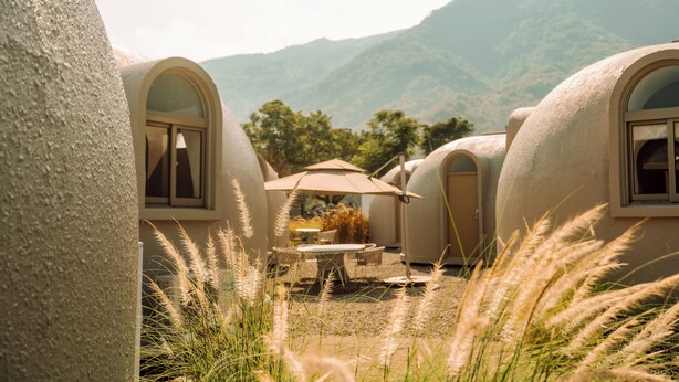A series of dome-shaped accommodations with arched windows, a central table with an umbrella, and a natural landscape in the background. - BOHOLAND (Zhushan)