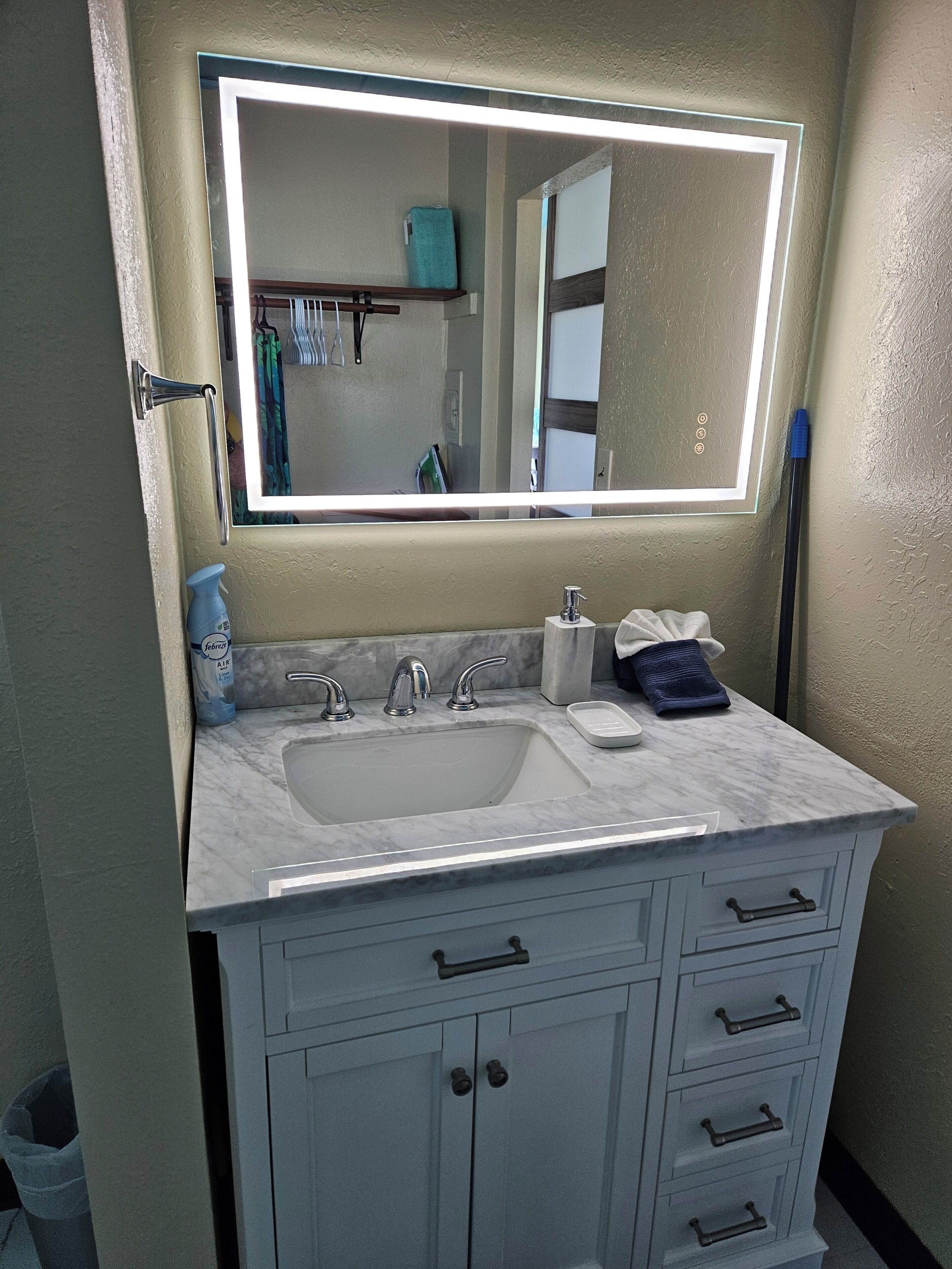 A bathroom with a white sink, a mirror with a light, and a cabinet with drawers.