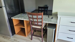 Une cuisine compacte dotée d’un plan de travail en granit, d’une chaise en bois, d’une poubelle et d’un meuble blanc avec des tiroirs.