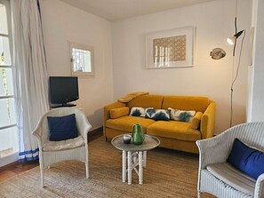 Ein Wohnzimmer mit einer Couch, zwei Sesseln, einem Couchtisch, einem Fernseher und einem Gemälde an der Wand.
