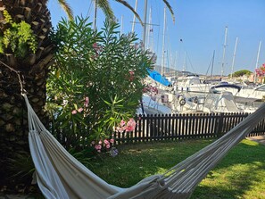 Un hamac installé dans un espace verdoyant, avec vue sur une marina où sont amarrés de nombreux bateaux.