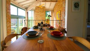 Un comedor con una mesa de madera dispuesta para cuatro personas, rodeado de paredes de ladrillo y ventanas amplias.