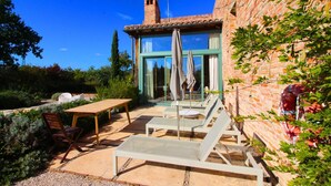 Un patio con sillones de descanso y una mesa, un muro de ladrillo y una puerta de vidrio que da a un espacio interior.