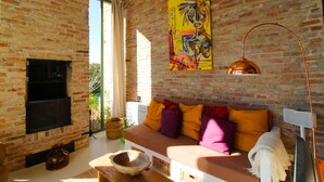 Una sala de estar acogedora con pared de ladrillo, un cuadro abstracto de colores, un sofá con cojines llamativos, una mesa de centro de madera y una lámpara de pie moderna.