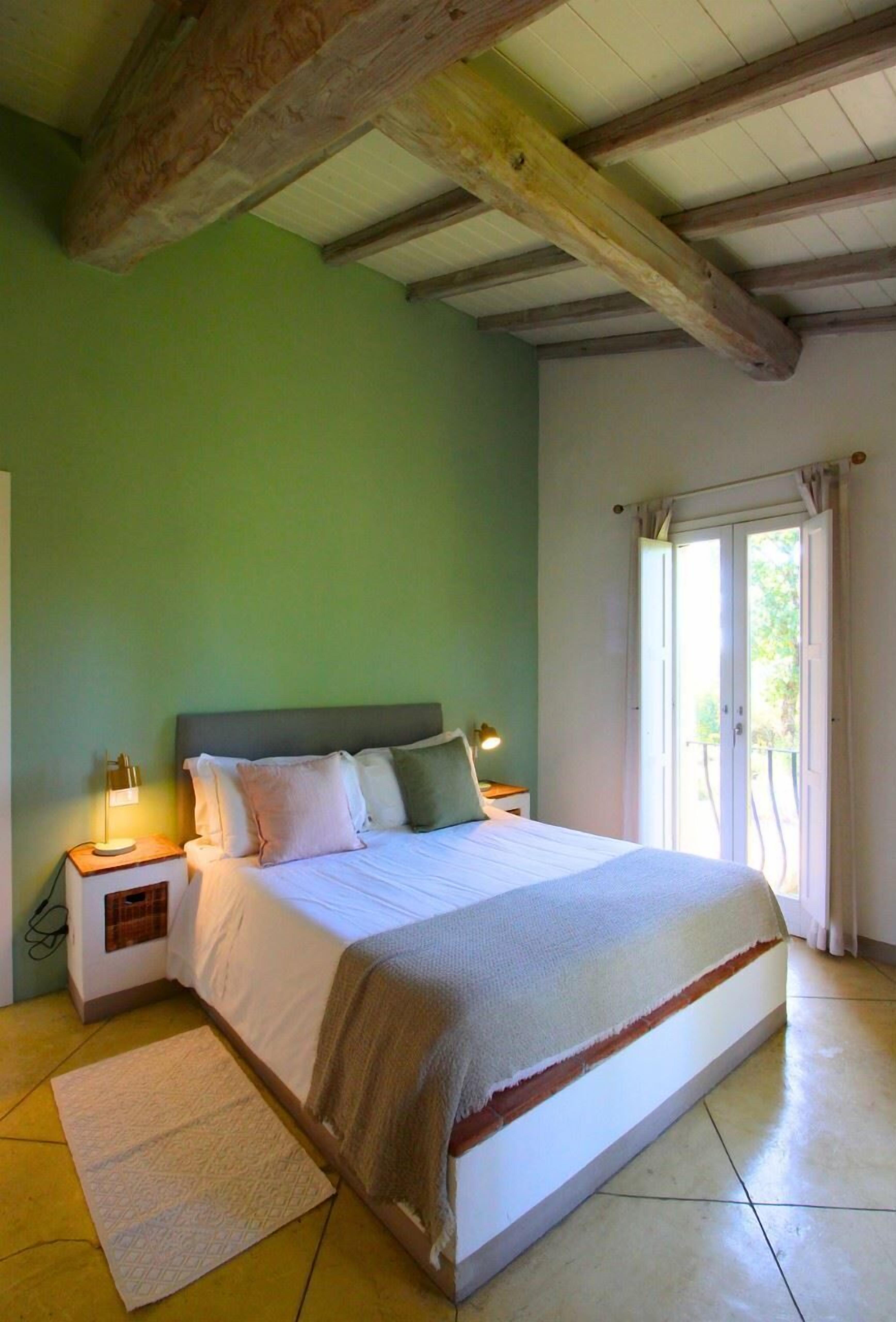 Un dormitorio con una cama, mesitas de noche, una lámpara y vistas al exterior a través de una puerta.