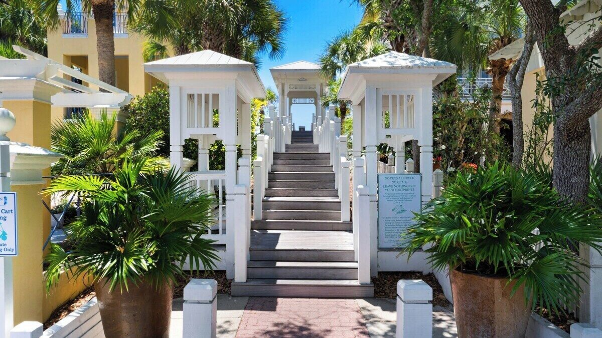 A staircase leading to a gated entrance with white railings and potted plants on either side.